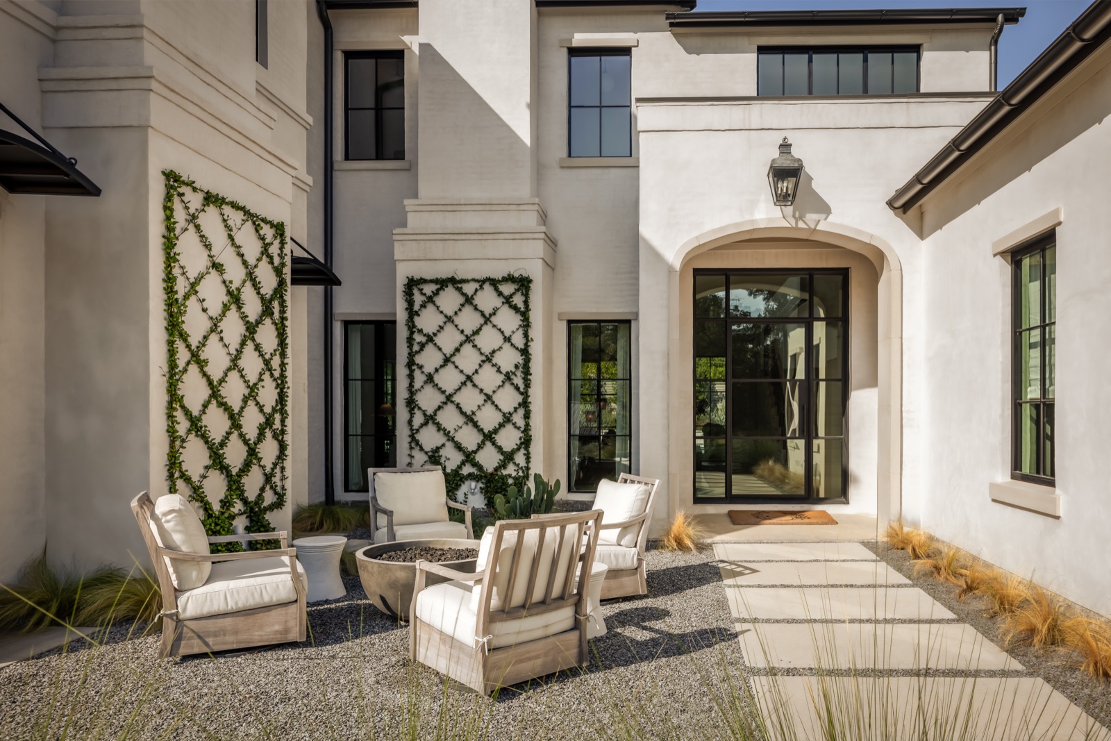 Courtyard with a black steel arched entry door and slim steel casement windows on a white stucco home.