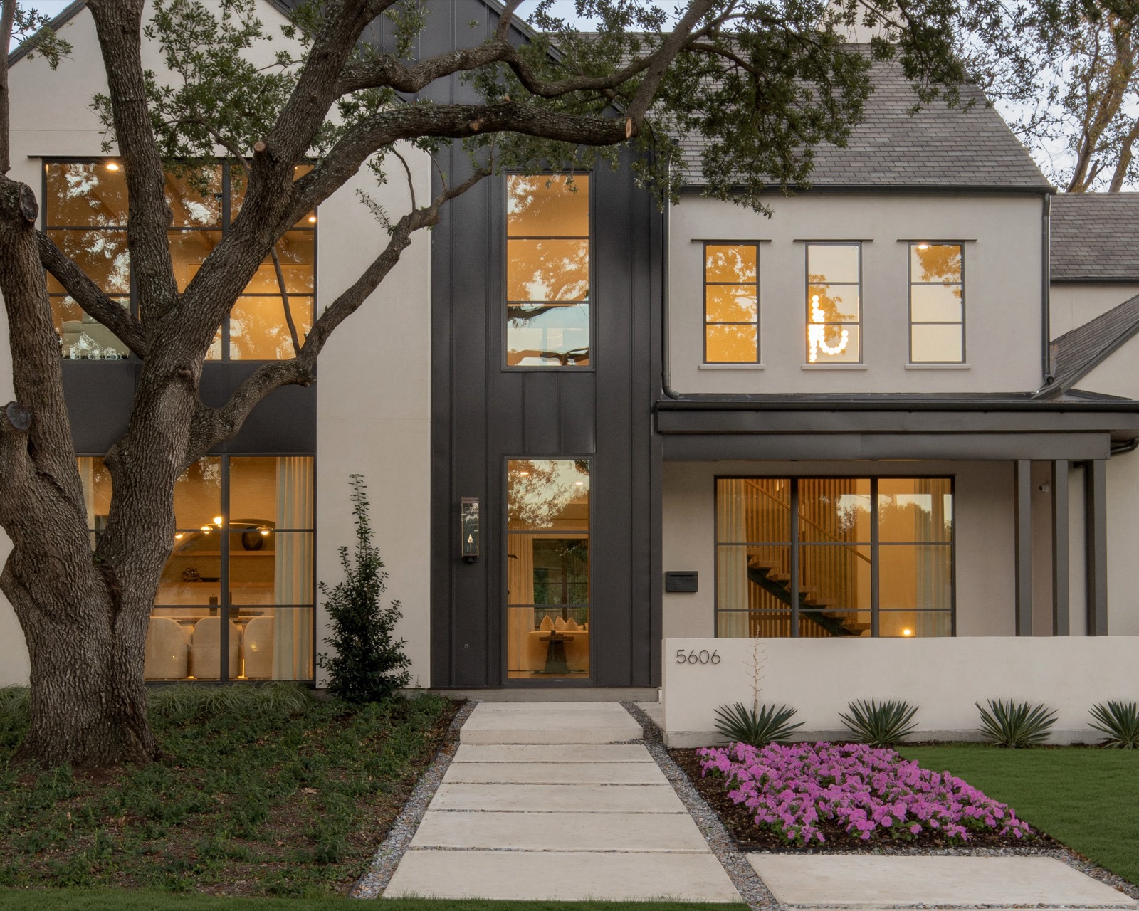 Blackened steel entry door and floor-to-ceiling steel windows on a white contemporary facade at dusk.